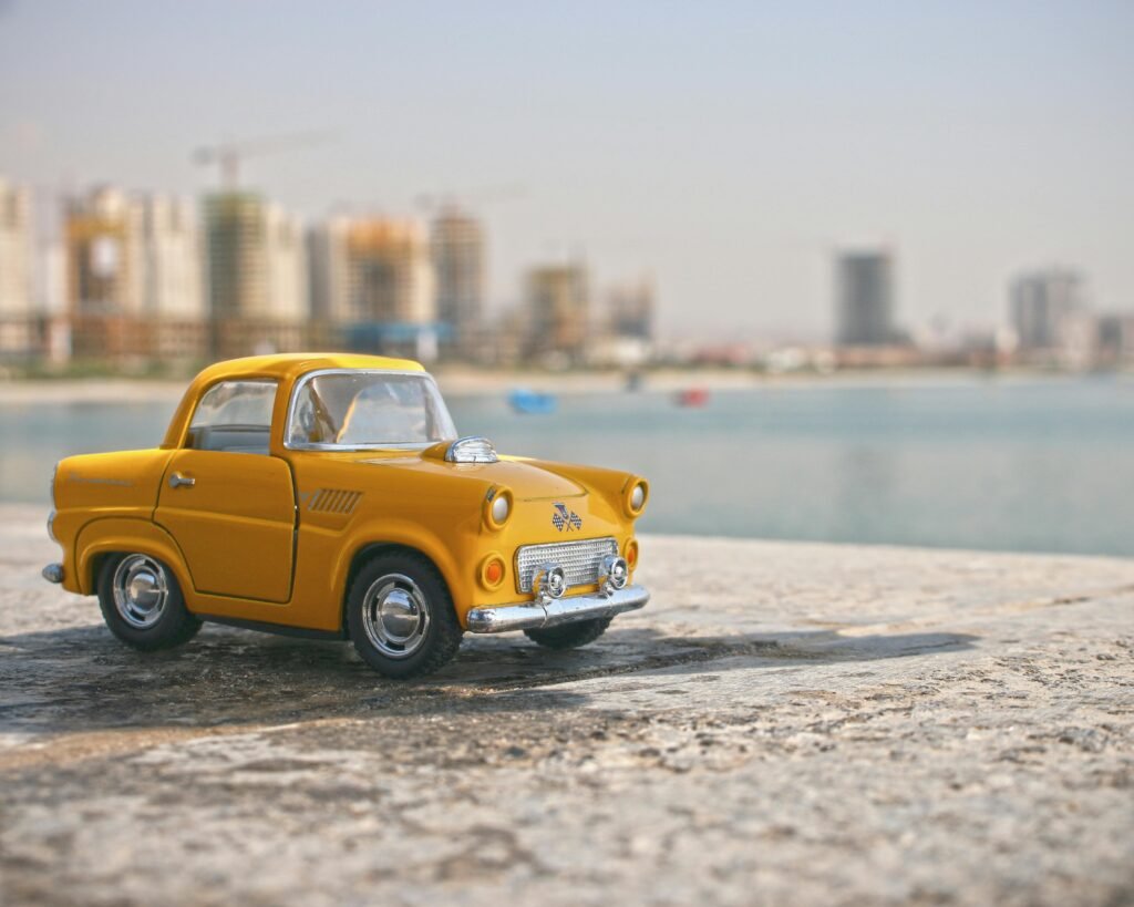pexels-photo-243206-243206 A bright yellow toy car set against a blurred city skyline beside a water body.